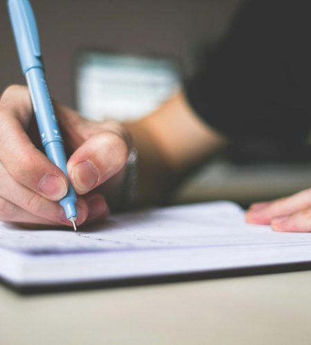 Close-up of hand writing in notebook using a blue pen, focus on creativity.